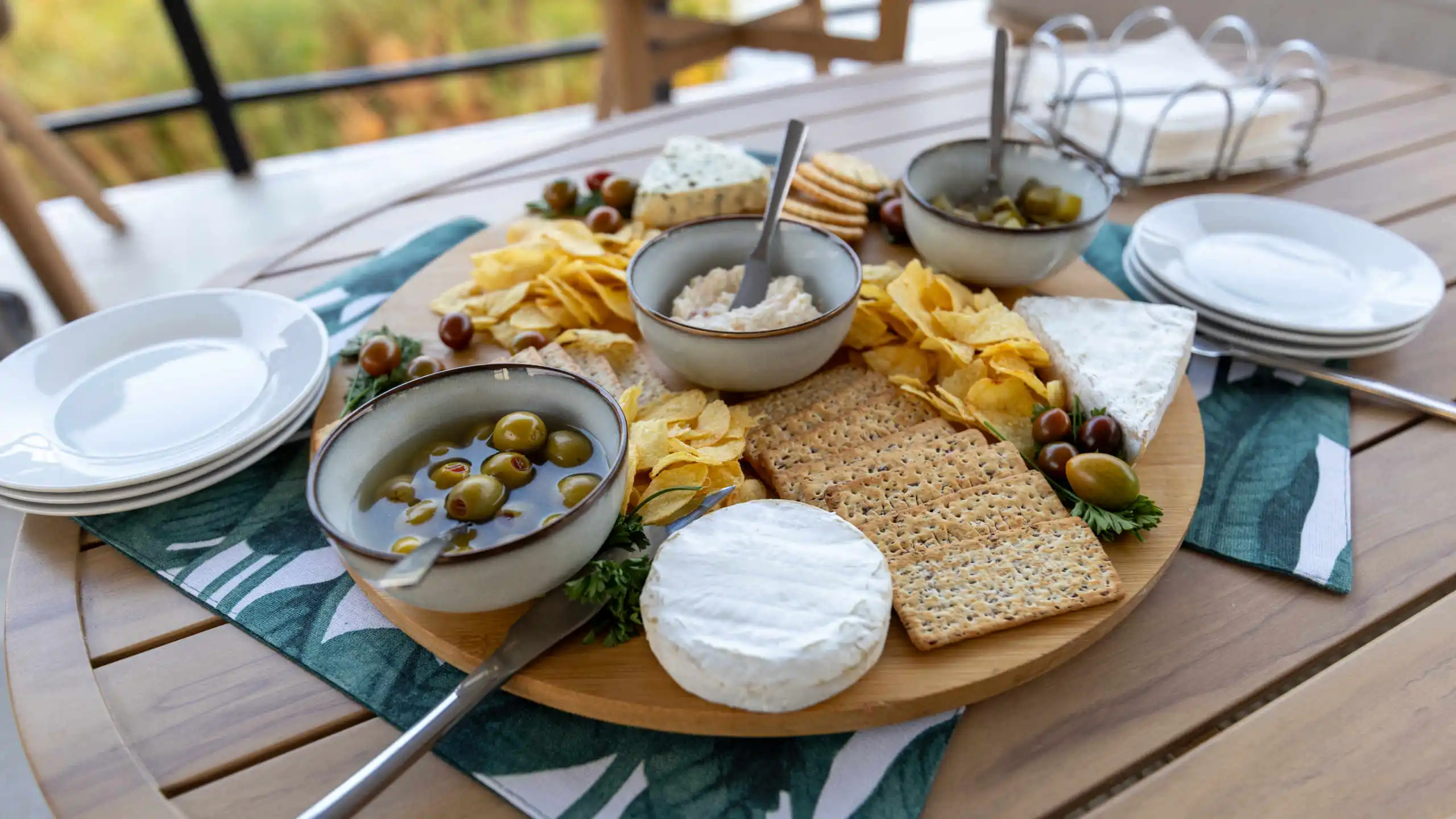 Delicious snack platter on the Ngwezi Houseboat featuring a variety of cheeses, crackers, olives, chips, and fresh grapes, perfect for a relaxing cruise on the Okavango Delta with stunning views.