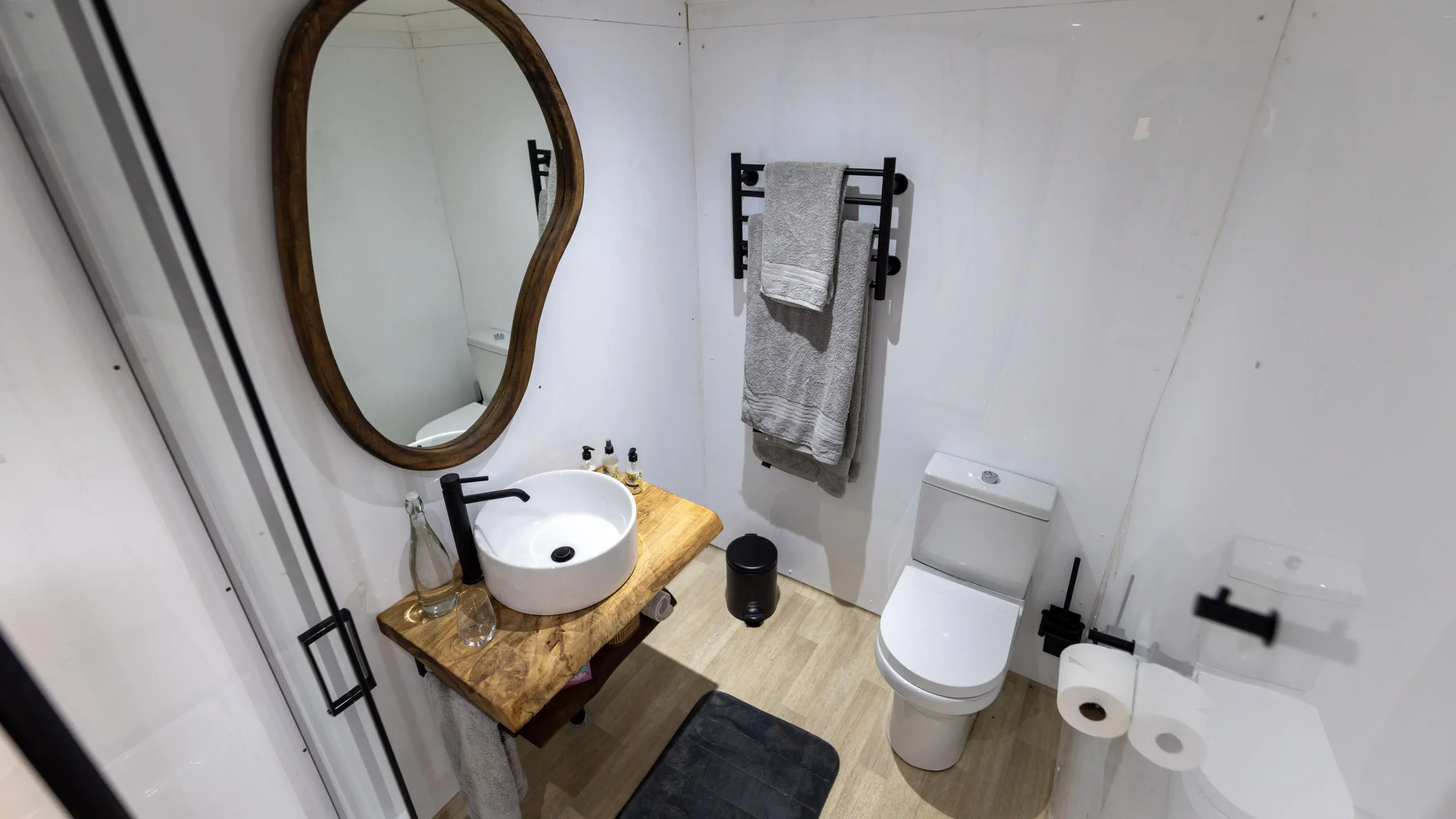 Modern and stylish bathroom on the Ngwezi Houseboat, featuring a sleek sink with a wooden countertop, a mirror, towels, and a white toilet, offering a comfortable and elegant experience while cruising the Okavango Delta.