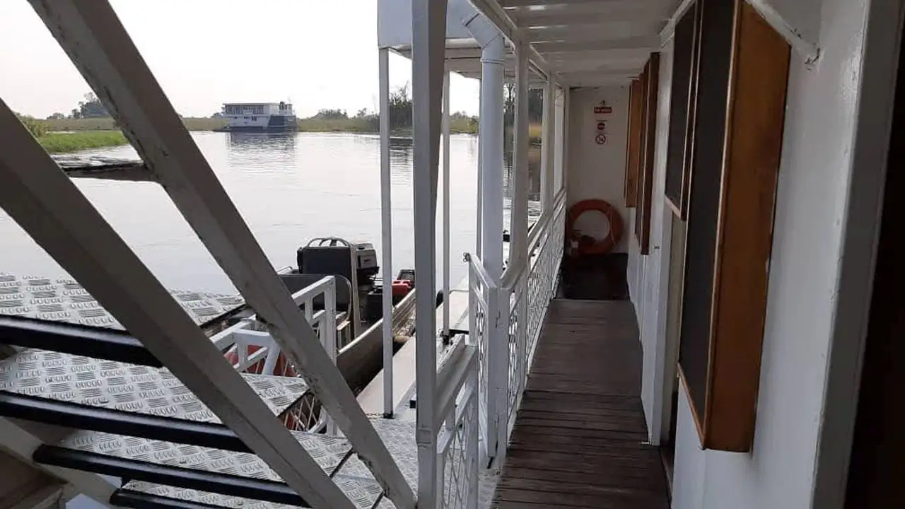 View of the exterior corridor of the Inkwazi Houseboat, showcasing the walkway along the boat with a nearby tender boat visible, providing guests easy access to the Okavango Delta's waters.