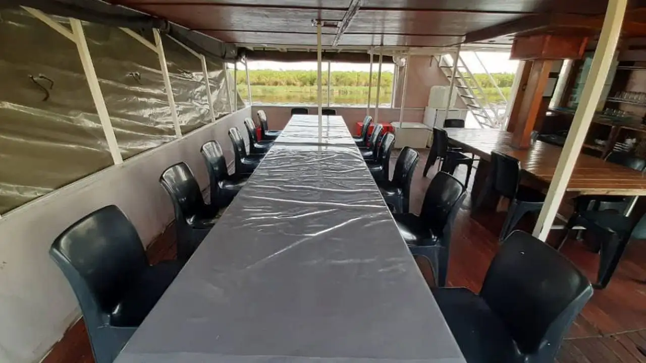 Interior view of the dining and seating area on the Inkwazi Houseboat, featuring a long table with chairs, offering guests a comfortable space to enjoy meals while cruising the Okavango Delta.