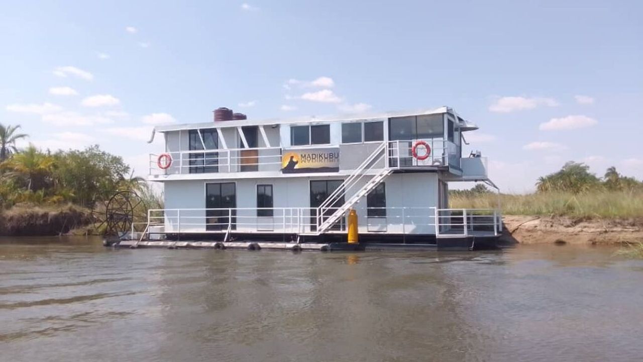 The Madikubu Houseboat cruising along the waterways of the Okavango Delta, featuring modern amenities and a spacious design for a unique water-based experience.