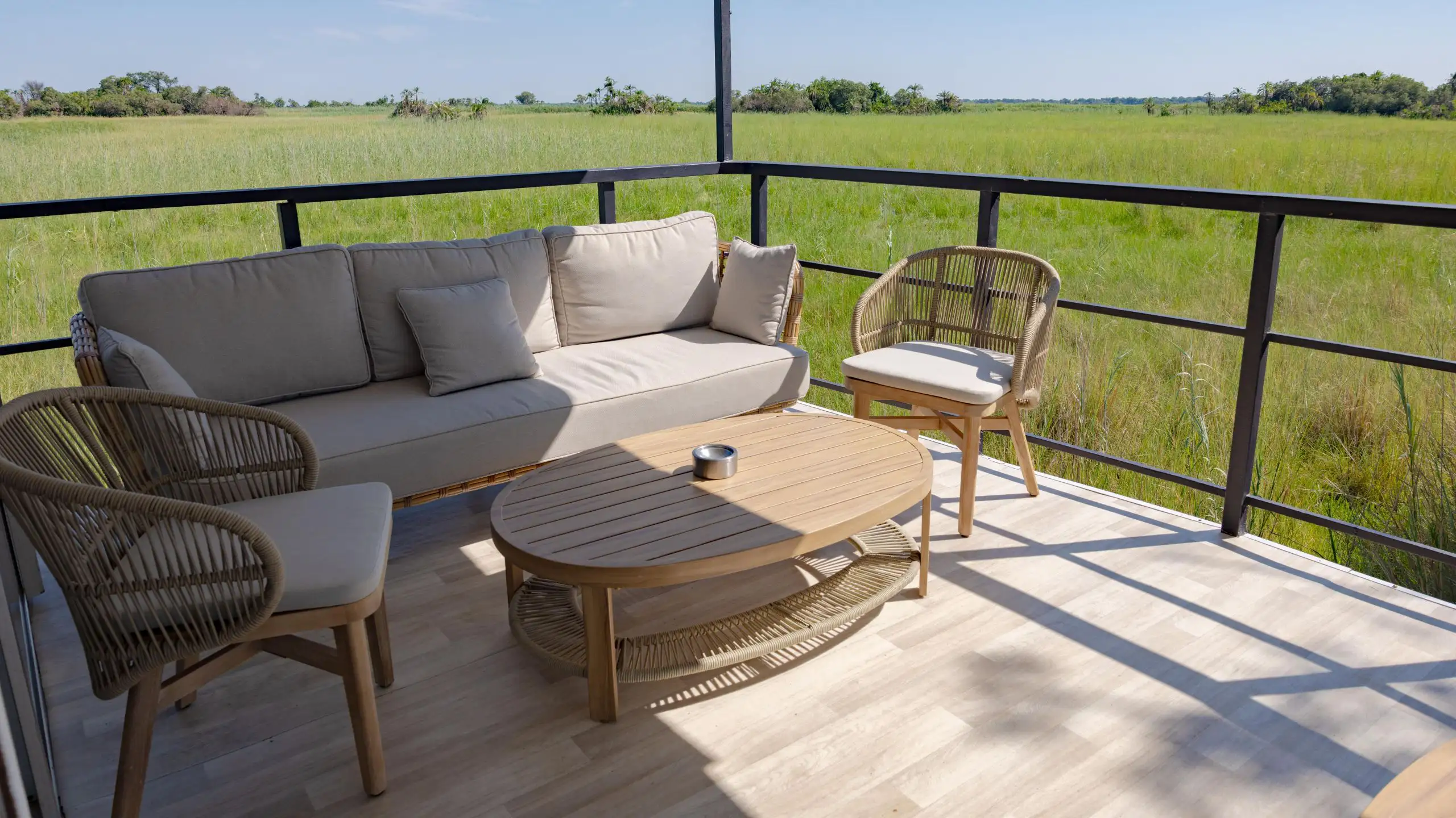 Ngwezi houseboat deck featuring a cozy seating area with a couch, chairs, and a wooden coffee table, offering a stunning view of the expansive Okavango Delta.