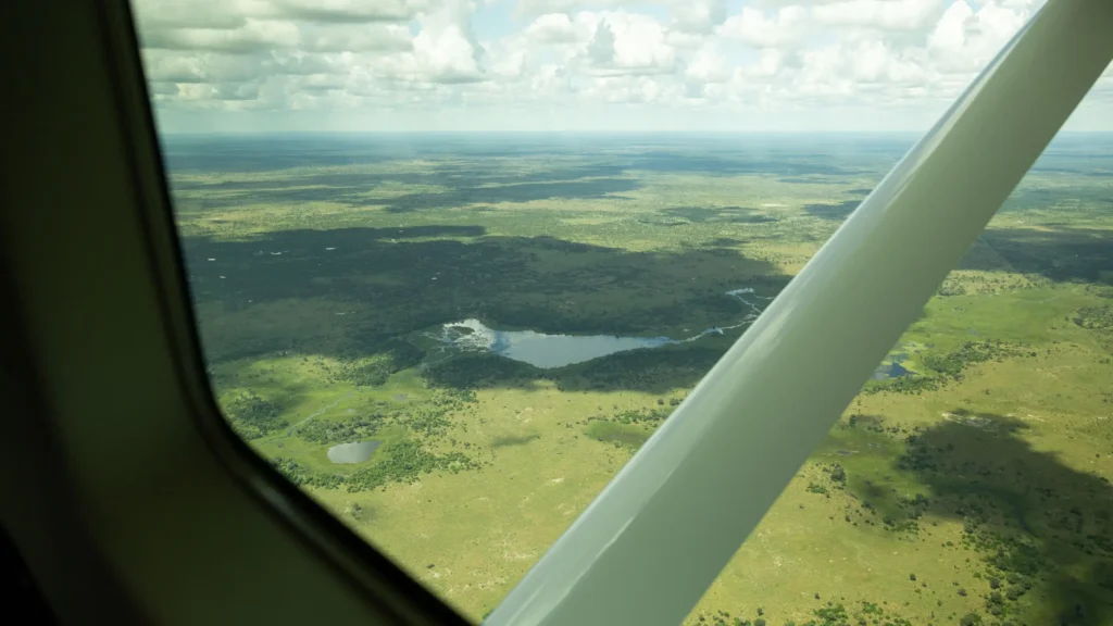 Aerial view of the Okavango Delta in Botswana, showcasing vast green landscapes, waterways, and a small water body, as seen from a light aircraft window.