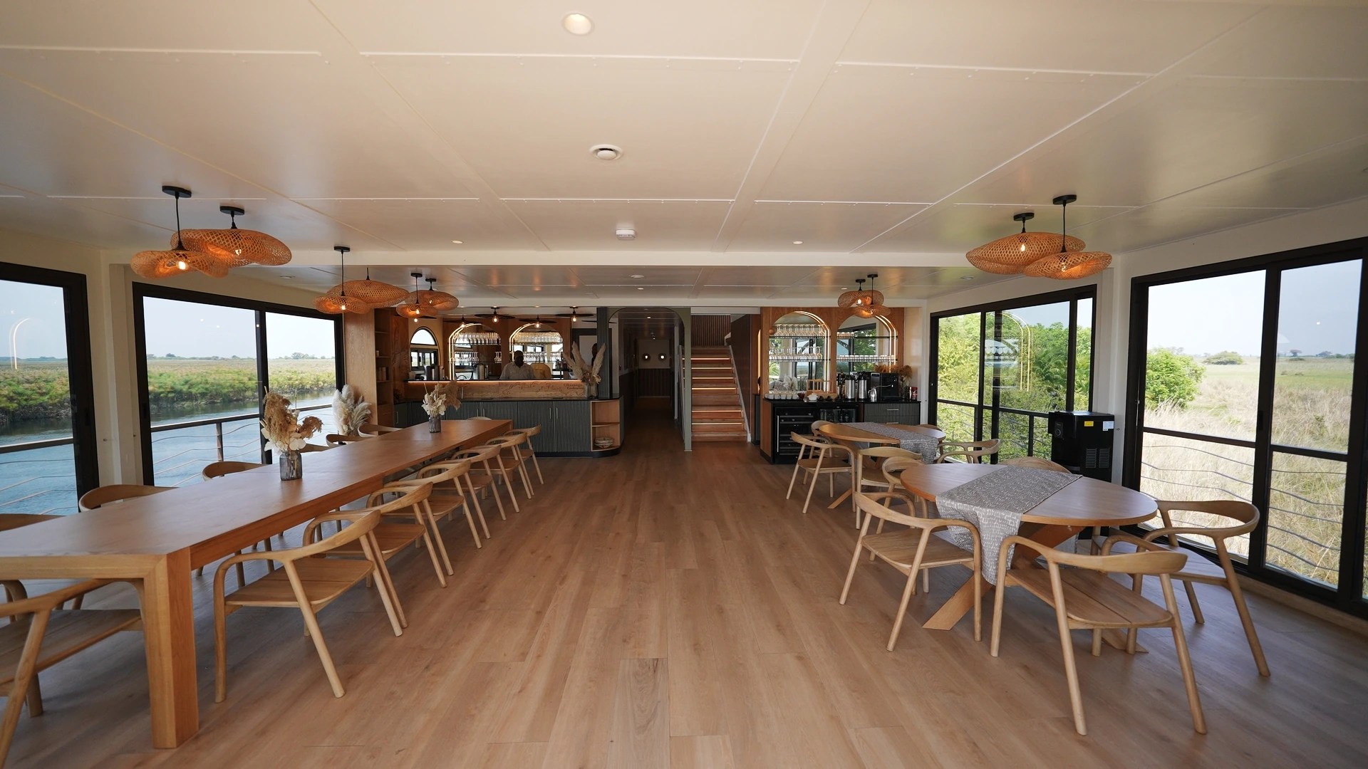Lounge and dining area aboard the Okavango Endeavour, with panoramic windows over the delta